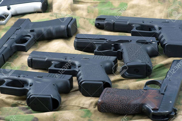 Several black handguns are laid out on a camouflage-patterned fabric surface.
