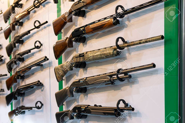 Multiple rifles are displayed horizontally on a wall-mounted rack, each secured with a lock around the trigger area.