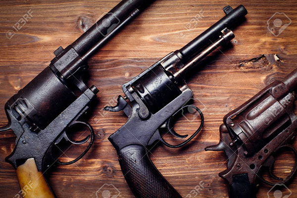 Three vintage revolvers are displayed on a wooden surface, shown from above with handles and barrels visible.